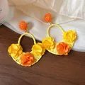 Close-up of yellow and orange raffia earrings with handmade ribbon flowers on wood. - Yellow