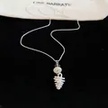 Close-up detail of a delicate white pinecone pendant necklace on a black velvet background - Pinecone Pendant / Silver