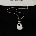 Close-up detail of a minimalist teardrop pendant necklace on a elegant black background - Oval Geometric Pendant / Silver