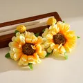 Nahaufnahme gelber Baststoff-Ohrringe in Blumenform auf einem Holzdisplay - Gelb
