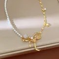 Close-up of elegant gold-plated bowknot necklace with pearls and floral details - Gold White