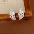 Vista macro detallada de pendientes de plata en forma de pluma con diamantes brillantes. - Estilo de Pluma / Plateado