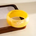 Detail view of yellow iridescent resin bangle with holographic finish on wooden tray - Yellow