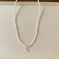 Close-up detail of pearl necklace with bow-shaped zircon pendant and soft textile backdrop - Bow Pearl Pendant Necklace / White