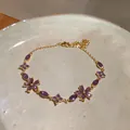 Macro detail of elegant purple zircon flower charms on a minimalist gold-plated bracelet - Purple