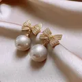 Detailed close-up view of elegant gold-toned zircon bow earrings with large lustrous drop pearls - Gold Bowknot Pearl Earrings (HE32345) / White