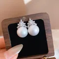 Close-up detail of elegant pearl stud earrings with sparkling zircon crown top - White