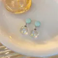 Dettaglio macro di orecchini a sfera in vetro trasparente con pois colorati e perni verdi - Blu Bianco