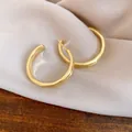 Dettaglio di eleganti orecchini a cerchio a C in oro opaco su morbida seta rosa - Oro
