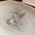 Close-up of silver-toned asymmetric starfish and shell drop earrings on a white plate. - Silver Asymmetric Ocean Element Style (28#)