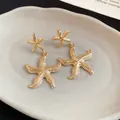 Detailed close-up of textured golden starfish dangle earrings on a white ceramic tray - Starfish Design Embossed Texture (29#)