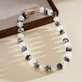 Detail of marbled acrylic round bead necklace with gold spacers on wooden tray. - Black Clear Marbling