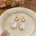 Close-up of elegant gold stud earrings with irregular white baroque pearls on a dish. - Large / Gold