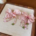 Close-up detail showing pink fabric flower earrings with delicate beads and green leaf charms - Earrings / Pink