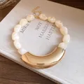 Close-up of marbled acrylic beads and curved gold metal pendant necklace details. - Beige