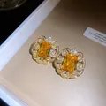 Gros plan de boucles d'oreilles en dentelle dorée avec une gemme rectangulaire jaune - Paire de Boucles d'Oreilles / Or-Jaune