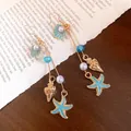 Macro view of blue enamel starfish and shell charms on golden dangle earrings - Hook Style / Gold-Blue