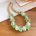 Close-up of acrylic green flower and gold beaded necklace on a wooden surface - Green