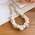 Close-up of acrylic oval bead necklace with white floral accents and gold beads. - Khaki