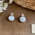 Detailed macro view of minimalist gold stud earrings with white cat eye stone and zircon - Round Cat's Eye Style / Gold