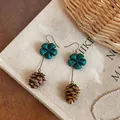 Detailed view of teal flower and brown pinecone drop earrings on linen background - Blue and Coffee