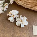 Elegante weiße Blütenblatt-Ohrclips mit Perlen auf einer rustikalen Holzfläche. - Feder-Ohrclip / Gold-Weiß
