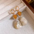 Nahaufnahme der Maillard-Retro-Resin-Ohrringe mit Marmorierung und goldenen Creolen. - Beige