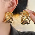Detailed view of chunky gold hollow knot stud earrings shown on ear and held by hand. - Silver Needle / Gold