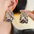 Close-up of silver-colored hollow woven C-shaped stud earrings on ear - Silver Needle / Silver