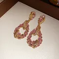 Elegant gold-tone feather teardrop earrings with sparkling pink oval crystals close-up. - Gold-Pink