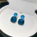 Close-up view of elegant square blue crystal stud earrings presented in a white jewelry box. - Stud Earrings / Silver-Blue