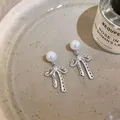 Close-up of elegant silver bow earrings with pearl accents on a ceramic plate - Bow Knot Pearl (HE27751) / Silver