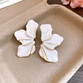 Close-up of elegant gold-toned flower earrings with white enamel petals in a tray - White
