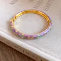 Detailed view of a purple enamel floral bangle with gold-tone metal and rhinestones - Green-Purple