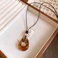 Close-up of amber resin oval pendant necklace on brown leather cord in a wooden jewelry box. - Irregular Oval Pendant (HN12382) / Coffee