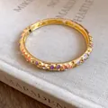 Detailed view of a gold-plated bangle featuring colorful enamel flowers and sparkling crystals - Gold, Purple and Orange
