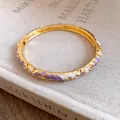 Macro view of a vintage gold-tone bangle with purple enamel flowers and sparkling rhinestones. - Gold-White-Purple