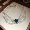 Detail view of a vintage three-layer pearl choker with a sparkling green triangle gem. - Necklace-White-Green