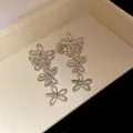 Macro view of silver hollow flower fringe drop earrings with three flower charms - Clip-On Earrings / Silver