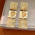 Detailed view of gold square drop earrings with unique embossed nose and ear motifs - Gold