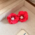 Macro detail showing vibrant red matte flower stud earrings with elegant pearl center - Pink