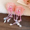 Detailed macro view of pink fabric flower earrings with beaded tassels and seashell charms. - Pink