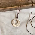 Close-up detail of a handmade round rattan woven pendant on a brown leather cord - Straw Hat Style