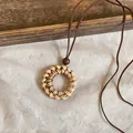 Close-up detail of a retro handcrafted rattan woven pendant necklace with brown leather cord - Round Style