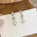 Detail shot of elegant silver drop earrings featuring star-shaped zircons and round pearls. - Silver