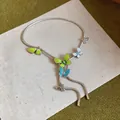 Macro detail of a silver snake chain necklace with colorful enamel butterfly charms on cream fabric - Multicolor