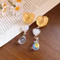 Primo piano di orecchini a cuore in resina e goccia d'acqua iridescente su legno - Stile con perno dell'orecchino in argento / Giallo-Bianco