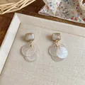 Close-up of cat's eye stud earrings with golden wire wrap and pearlescent disc charms - Silver Earring Post Style / White