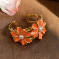 Close-up of elegant orange enamel daisy cuff bracelet with pearls on a rustic wood background - Orange