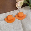 Gros plan de boucles d'oreilles géométriques en acrylique orange vif sur un coussin beige - Style d'Épissage de Demi-cercle Géométrique (HE33764) / Orange